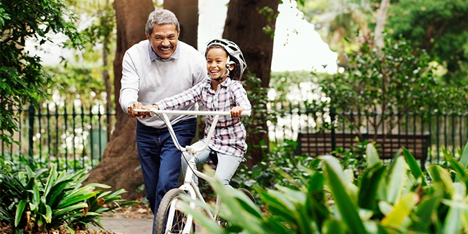 Little girl being taught how to ride a bicycle by her grandfather at the park