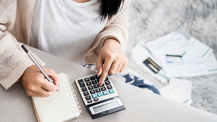 Woman writing list of debt on notebook and using calculator.