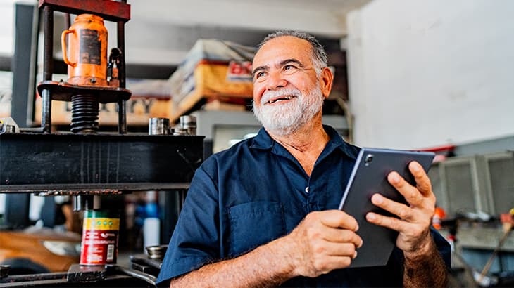 Smiling mechanic using a digital tablet in an auto repair shop.