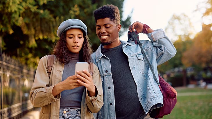 Young couple outdoors looking down together at a smartphone screen.