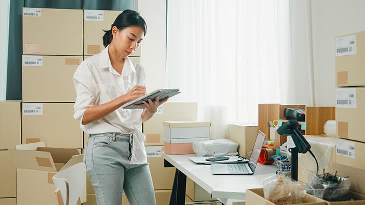 Woman in an office holding a digital tablet next to stacks of cardboard boxes.