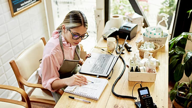 Small business owner working on a laptop and taking notes at an office desk.