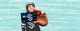 Woman wearing a helmet holding up a WaFd Bank Seattle Kraken debit card against a light blue patterned background.