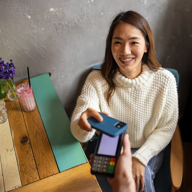 Customer smiling while making a mobile payment with her phone at a restaurant table.