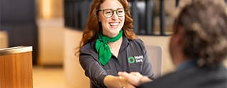 Representante sonriente de WaFd Bank con gafas y una bufanda verde hablando con un cliente.