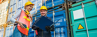 Two people in hardhats talking by shipping containers.