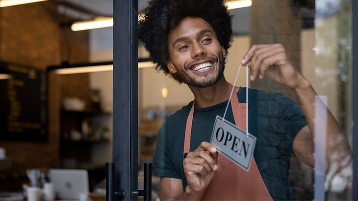 A young business owner smiling while hanging an open sign on the door.