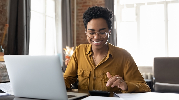 Mujer feliz con gafas usando calculadora y laptop para presupuestar.