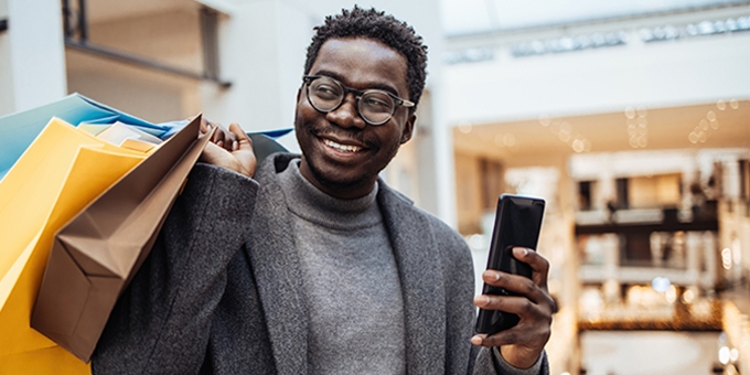 Man with shopping bags holding phone in big shopping mall.