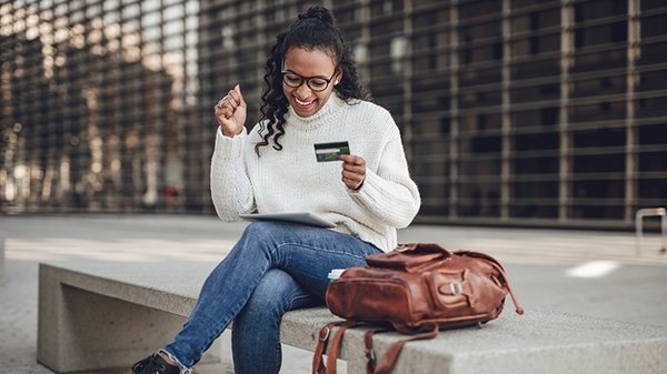 Young woman sitting outside with credit card in hand and tablet.