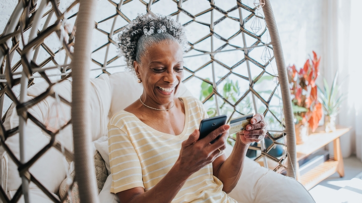 Woman using credit card holding her cell phone in living room.