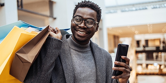 Man with shopping bags holding phone in big shopping mall.