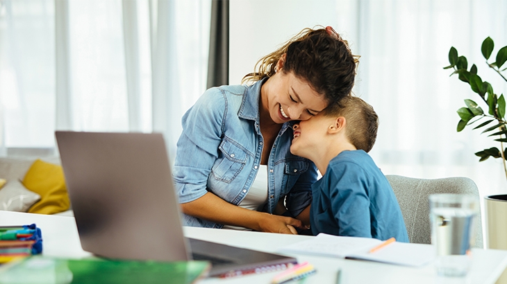 A mother and young son laughing while doing homework.