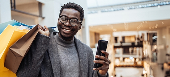 Man with shopping bags holding phone in big shopping mall.