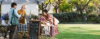 People buying flowers at an outdoor booth with a Zelle accepted here sign.