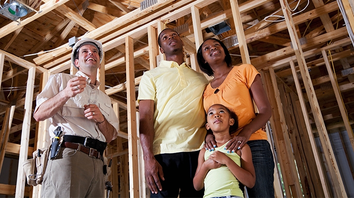 Happy young family in framed house with contractor.