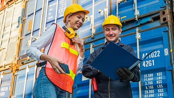 Two people in hardhats talking by shipping containers.