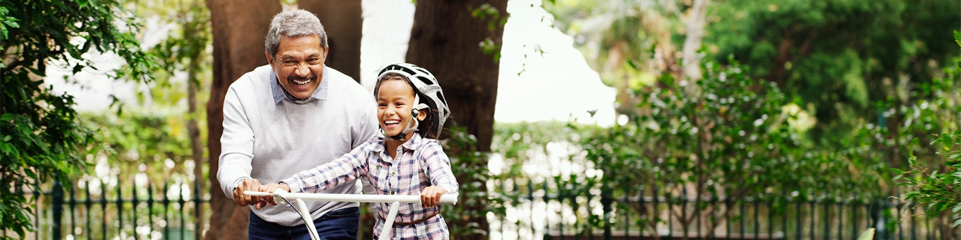 Little girl being taught how to ride a bicycle by her grandfather at the park.