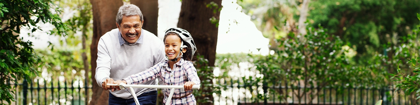 Little girl being taught how to ride a bicycle by her grandfather at the park