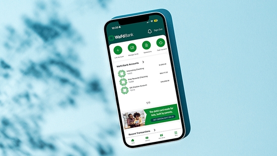 A smartphone displaying the WaFd Bank mobile app interface is positioned at a slight angle against a solid light-blue background with soft leaf shadows.
