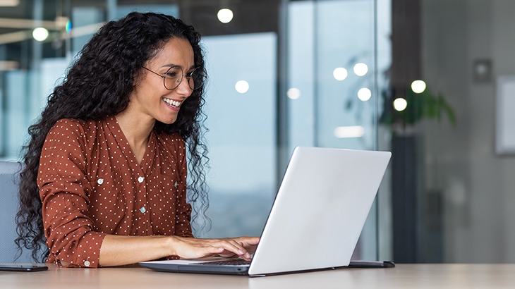 Happy businesswoman in an office working on a laptop.