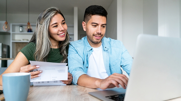 Happy couple at home paying bills online on their laptop