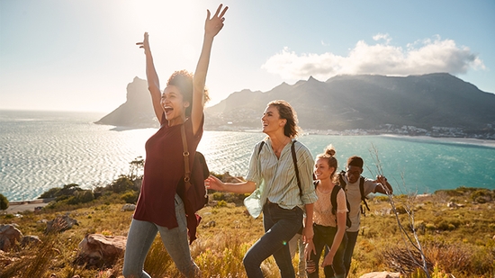 A group of friends cheerfully hikes along a scenic mountain trail overlooking the ocean.