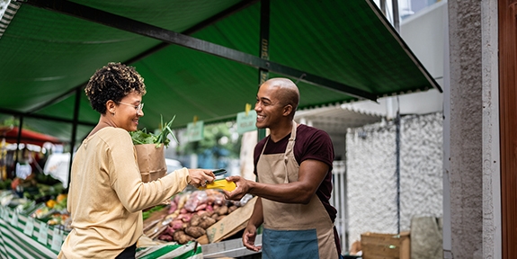 Woman checking out at vegetable stand with a mobile phone.