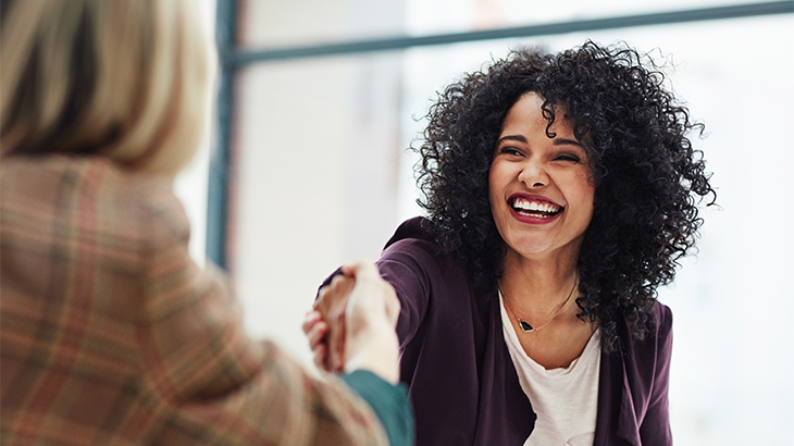 Businesswomen shaking hands while smiling.