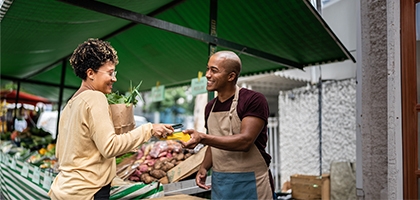 Woman checking out at vegetable stand with a mobile phone.