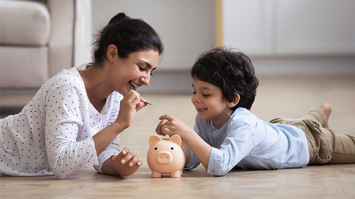 Mother teaching son about saving money, putting money in piggy bank.