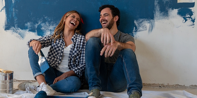 Couple laughing while painting a wall in their house