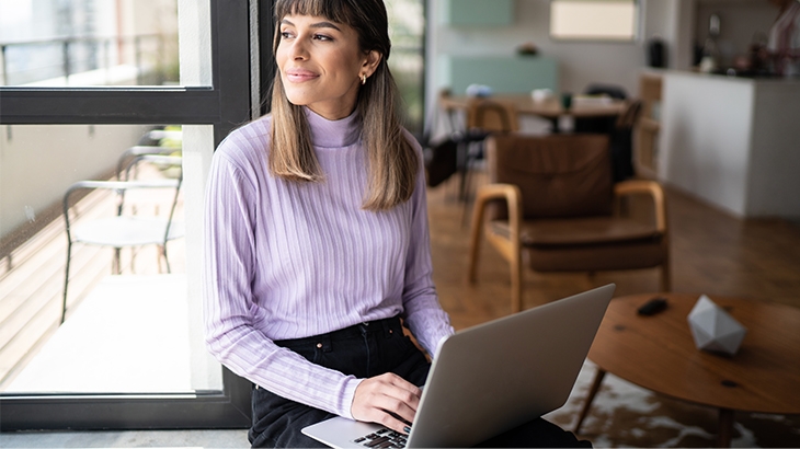 A woman sitting by the window while using laptop.