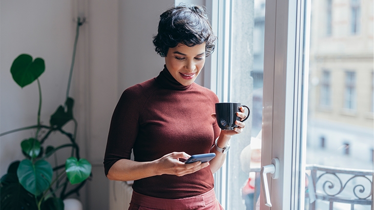 A businesswoman with a cup of coffee is checking her cell phone.