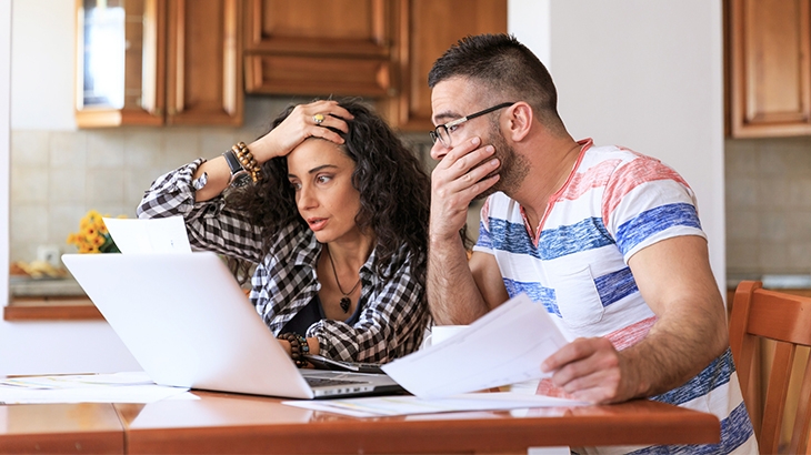 Couple sitting at table stressed looking at bills.