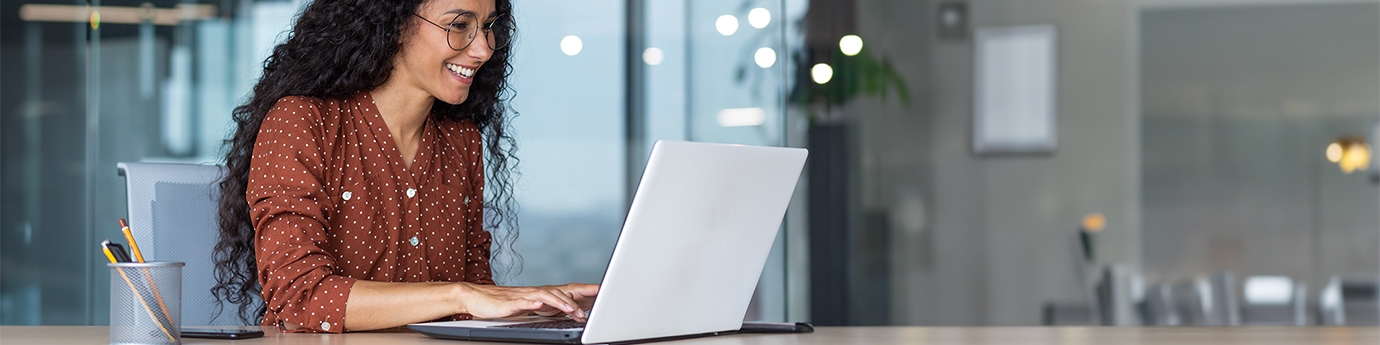 Happy businesswoman in an office working on a laptop.