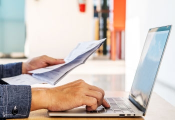 Closeup of a businessman holding documents and working on laptop at a desk
