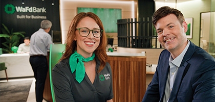 A smiling woman in a WaFd Bank uniform and a man in a blue suit sitting together inside a modern WaFd Bank branch.