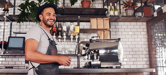 Happy young bar owner standing at the counter.