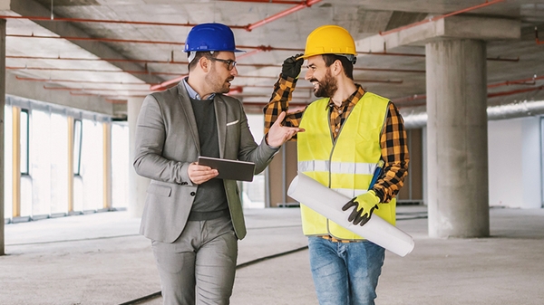 Construction worker and architect talking in building under construction.