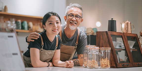 Father and daughter running their cafe, smiling at the counter. 