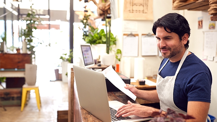 A male business owner working on a laptop behind a sales desk.