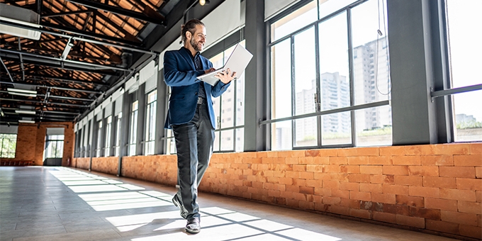 A Businessman walking through an empty office building, looking at his laptop.