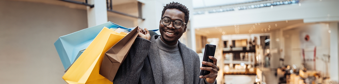 Man with shopping bags holding phone in big shopping mall.