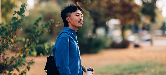 A man in a blue shirt holding a coffee cup while standing outdoors in a park setting.