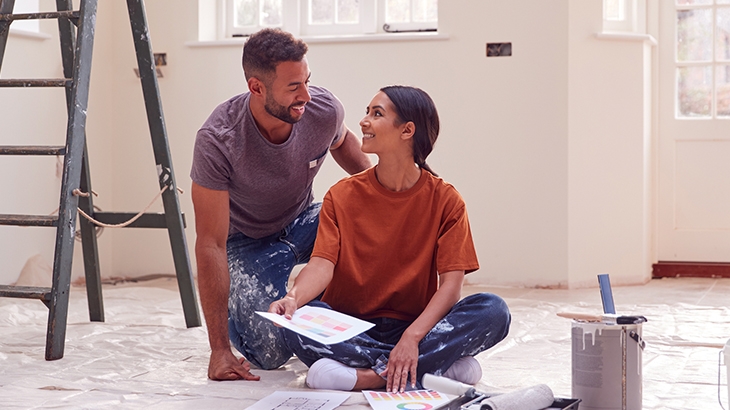 Couple Sitting On Floor With Paint Chart Ready To Decorate New Home.
