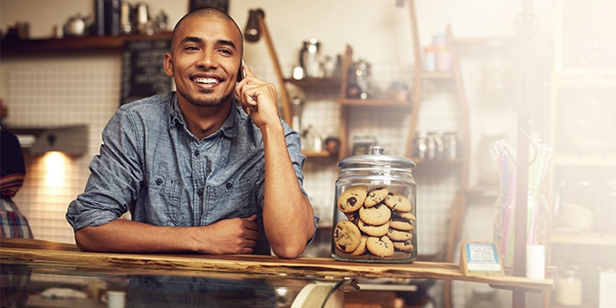 Young entrepreneur on his mobile phone at the checkout counter in his shop.