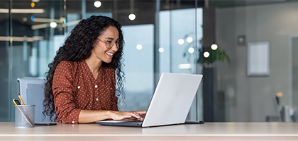 Happy businesswoman in an office working on a laptop.