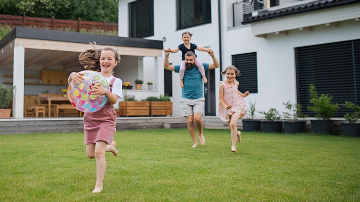 Father and children laughing and playing ball in the yard.