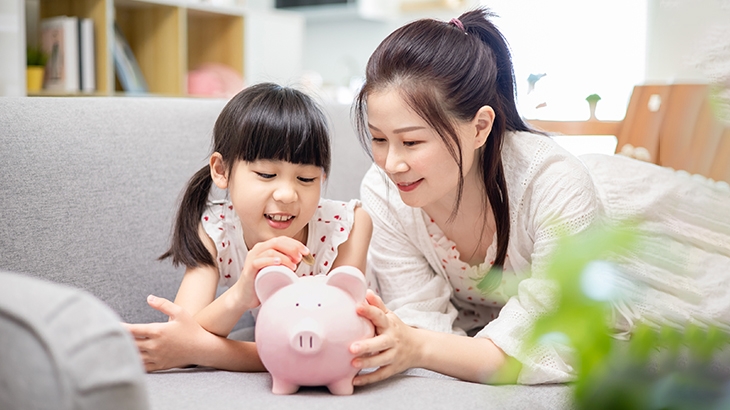 Madre e hija sonrientes poniendo monedas en una alcancía.